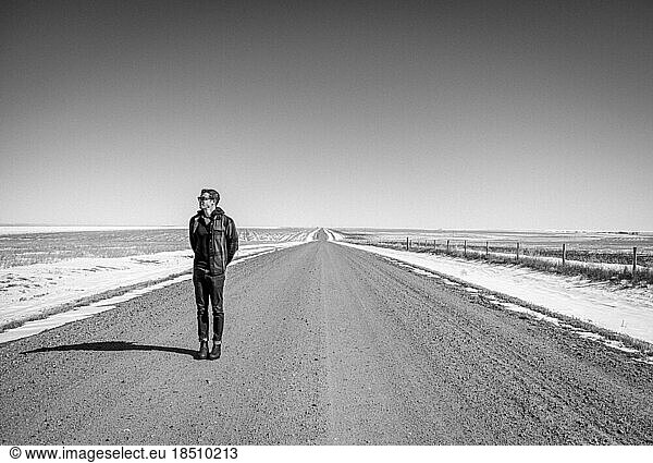 Man stands along long straight flat gravel road in Kansas in winter