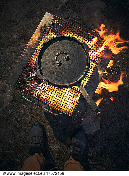 Man stands over a cast iron cooking over an open fire.