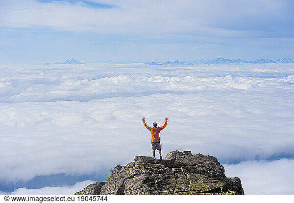 Man stretches arms overhead  mountain summit