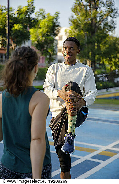 Man stretching legs with friend at sports court