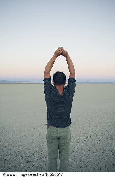 Man stretching with arms above head  facing the sunrise over expansive desert  Black Rock Desert  Nevada