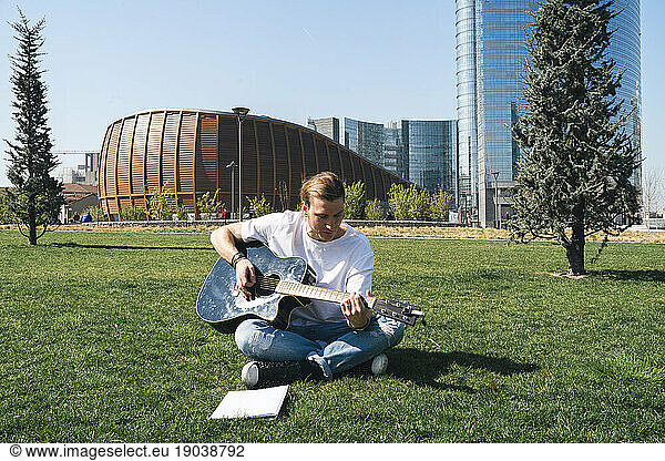 man studying music in urban garden playing guitar and reading script