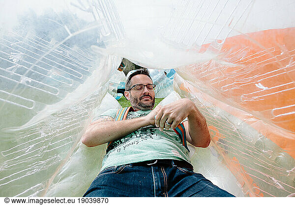 Man suits up and adjust straps of his bubble soccer inflatable ball