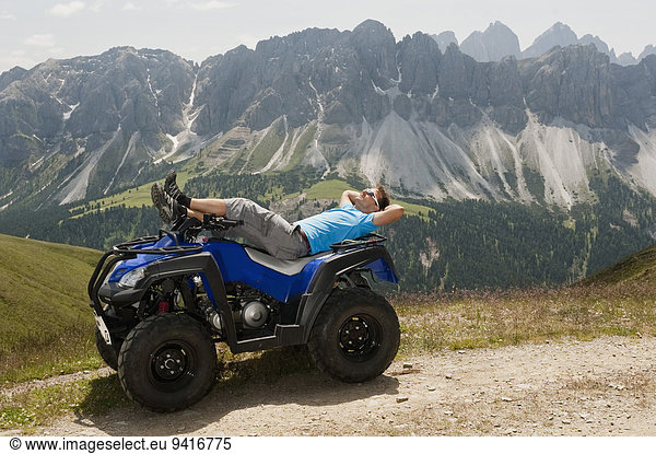 Man sunbathing on Quad bike in mountain landscape