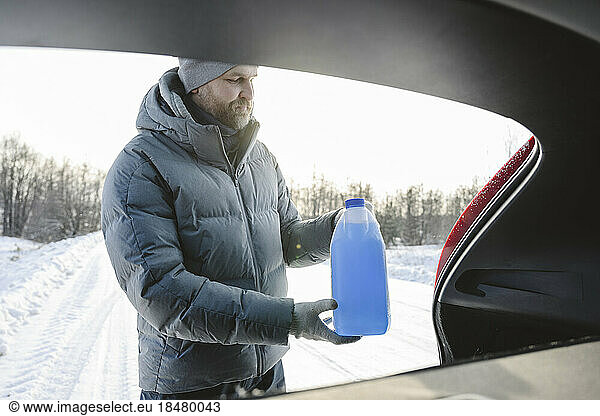 Man taking bottle of car anti-freeze liquid from trunk in winter
