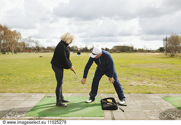 Man teaching golf to woman at driving range