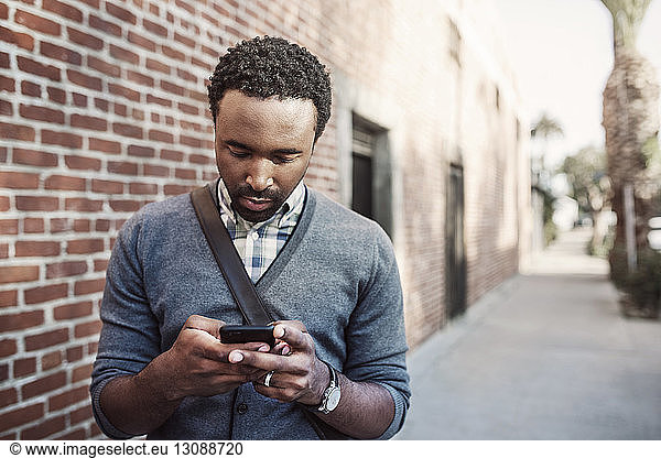 Man text messaging while standing on sidewalk