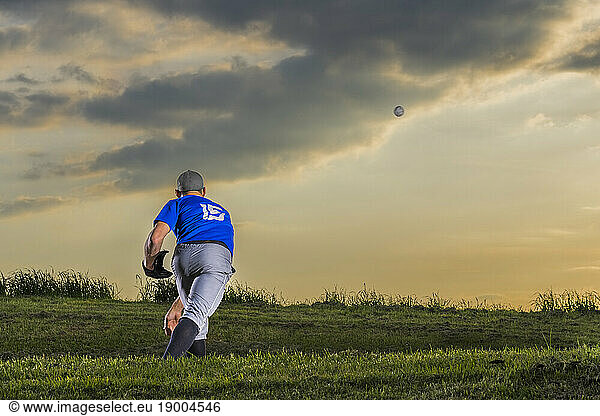 Man throwing baseball standing in grass at dusk