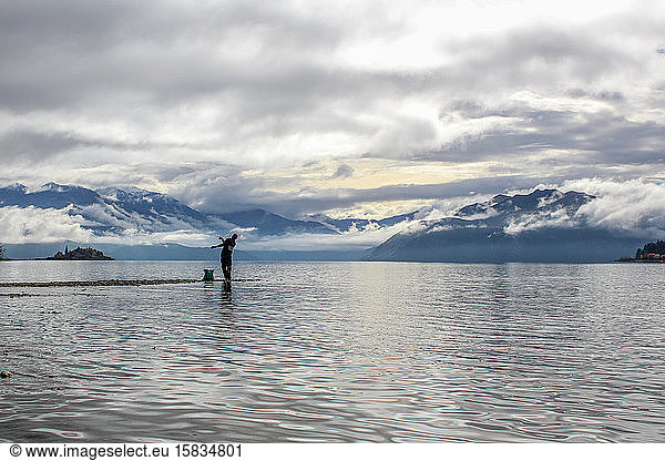 Man throwing rock into lake overlooking stunning New Zealand mountains