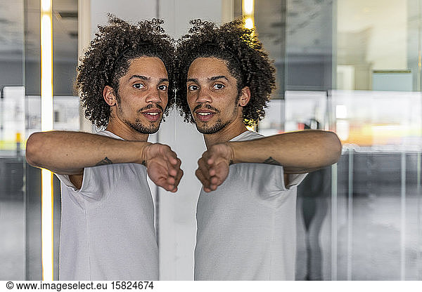 Man touching mirror images of himself on a glasspane