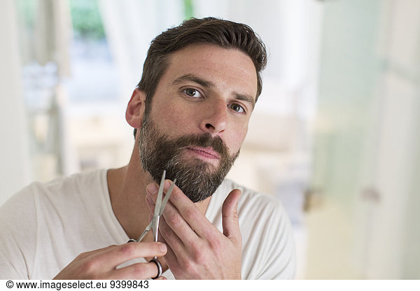 Man trimming beard in bathroom