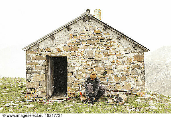Man tying shoe near brick house on mountain