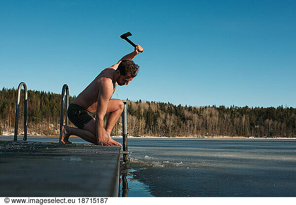 Man using an axe to break the ice in the sea to go cold water swimming