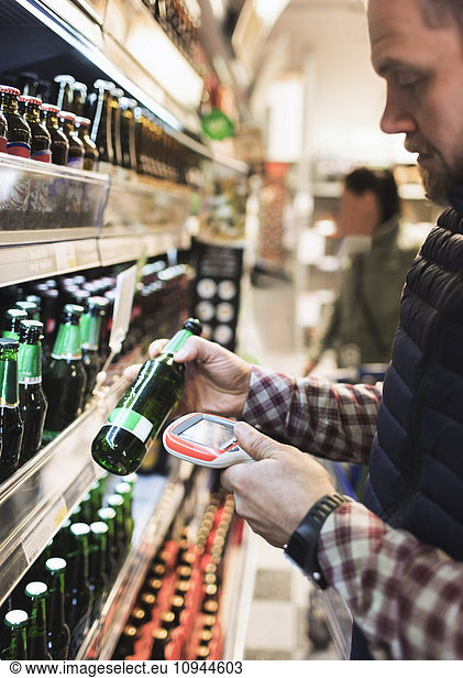 Man using bar code reader on beer bottle in supermarket