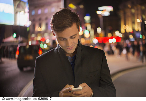 Man using cell phone on city street at night