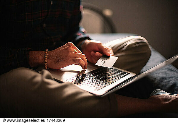 Man using credit card and laptop computer shopping online at home