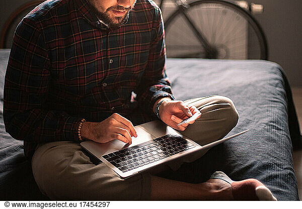 Man using credit card and laptop computer shopping online at home