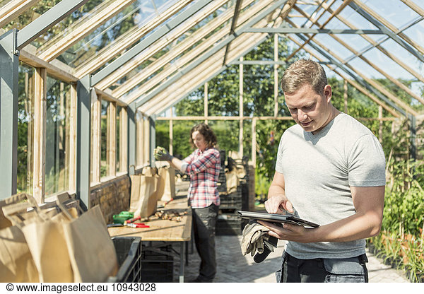 Man using digital tablet while woman working in greenhouse