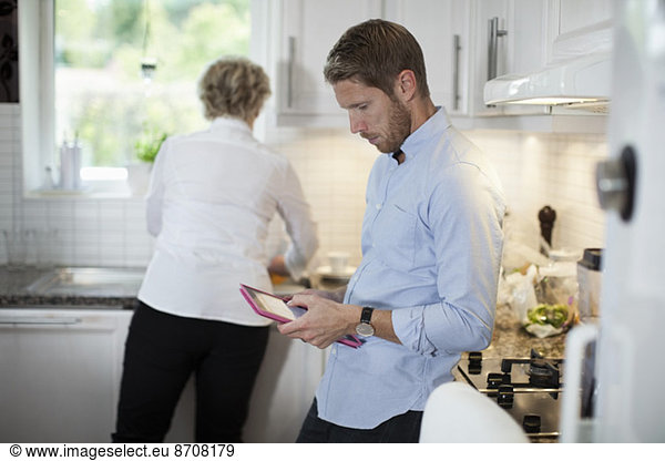 Man using digital tablet with mother cooking in kitchen