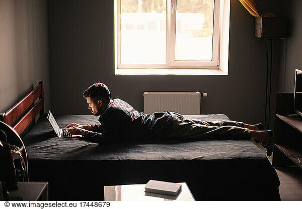 Man using laptop computer lying on bed at home