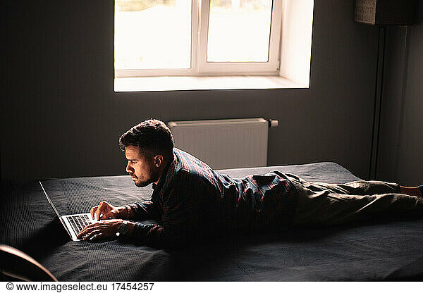 Man using laptop computer lying on bed at home