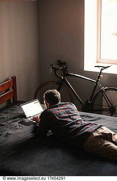Man using laptop computer lying on bed at home