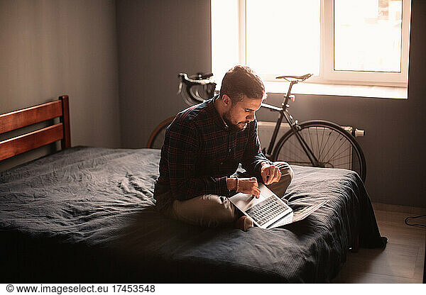 Man using laptop computer sitting on bed at home