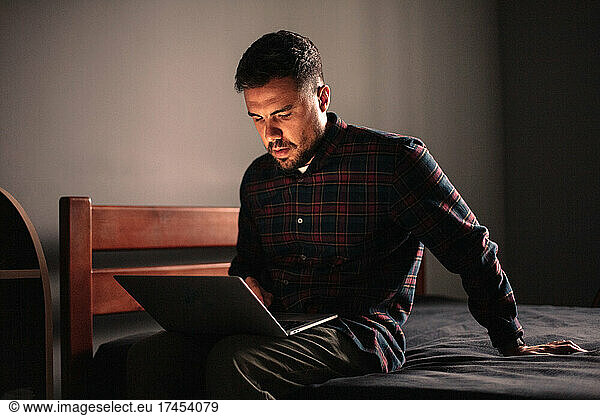 Man using laptop computer sitting on bed at home