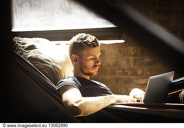 Man using laptop computer while relaxing in hammock