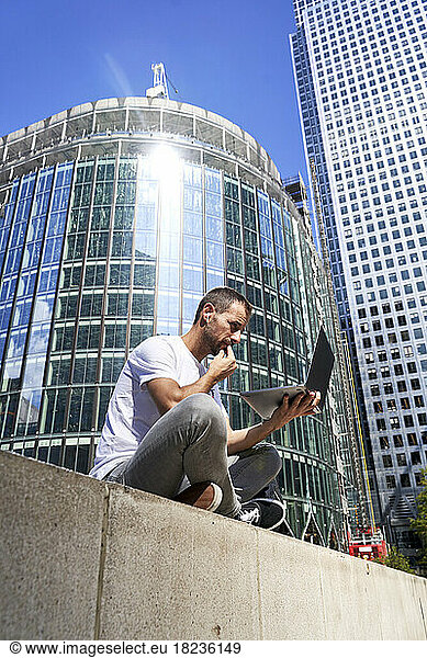 Man using laptop in city on sunny day