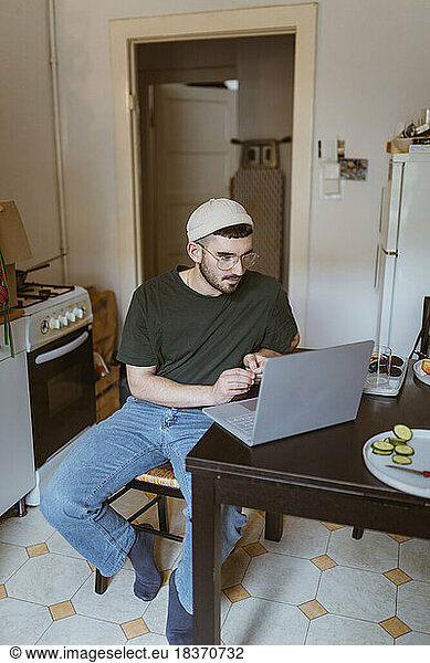 Man using laptop on dining table sitting in kitchen at home