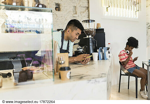 Man using mobile phone leaning on checkout in coffee shop