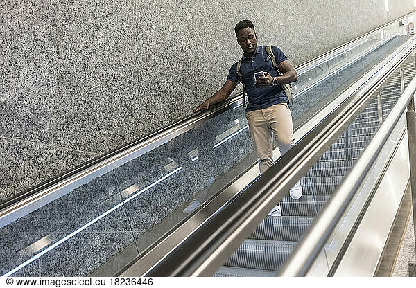 Man using mobile phone moving down on escalator