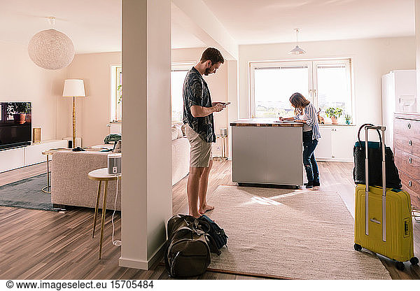 Man using mobile phone while woman filling form in apartment during vacations