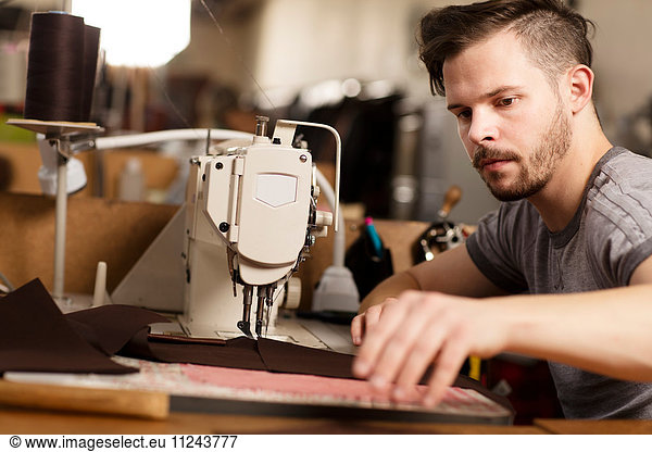 Man using sewing machine to sew leather in leather jacket manufacturers