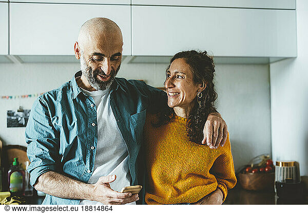 Man using smart phone by smiling woman in kitchen at home