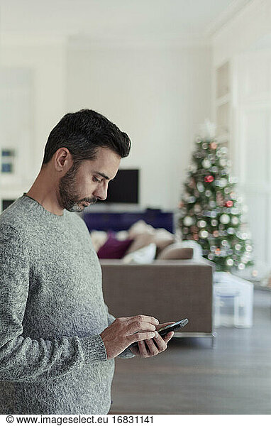 Man using smart phone in living room with Christmas tree