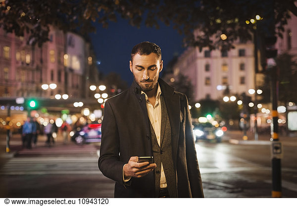 Man using smart phone on city street at night