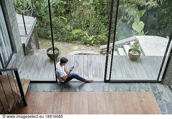 Man using smart phone sitting by glass door