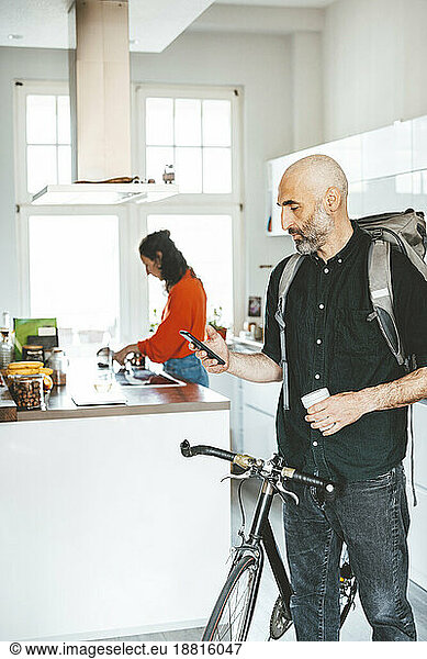 Man using smart phone standing with bicycle at home