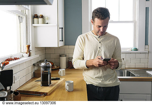 Man using smart phone while leaning by kitchen counter at home