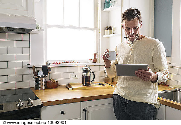 Man using tablet computer while leaning on kitchen counter at home