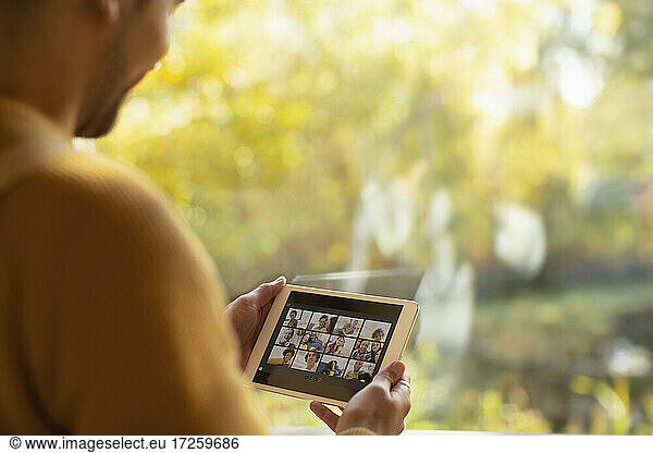 Man video chatting with friends on digital tablet screen at window