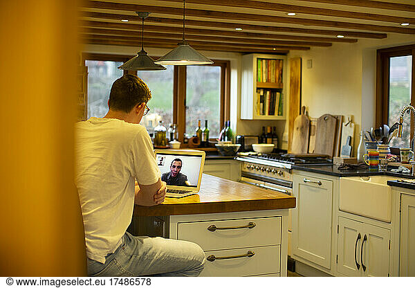 Man video conferencing with colleagues at laptop in kitchen