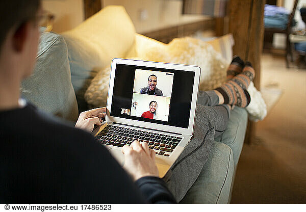 Man video conferencing with colleagues on laptop screen from sofa
