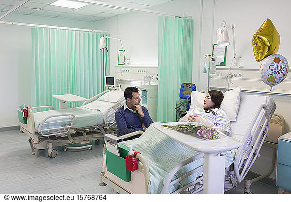 Man visiting  talking with wife resting in hospital ward