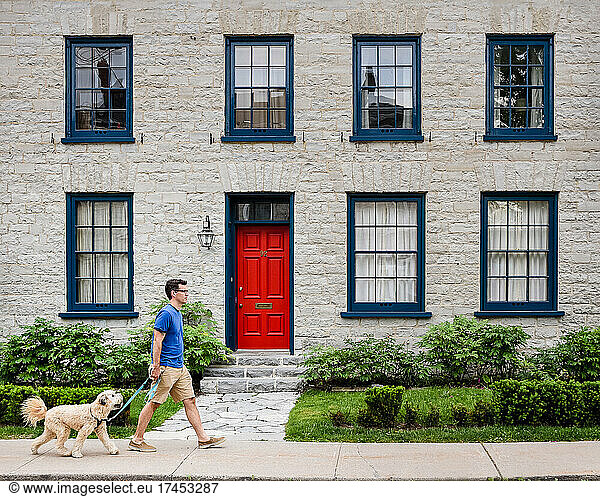 Man walking a dog in front of stone house with red door.