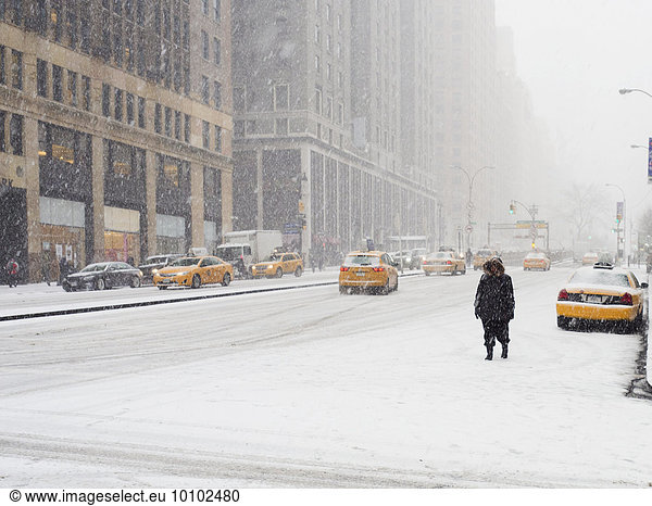 Man walking in a city in the snow during a blizzard  yellow taxis on the street.