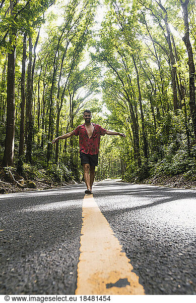 Man walking on road marking in front of trees