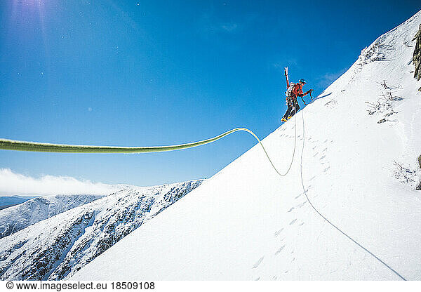 Man walking uphill with ice climbing tools and skis on his back